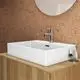 Weißer Waschtisch von Ideal Standard mit quadratischer Form, montiert auf einem Holzunterbau, ausgestattet mit einem modernen Wasserhahn und einem runden Spiegel im Hintergrund.